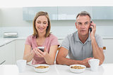 Couple using cell phones while having breakfast in kitchen