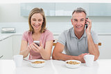 Couple using cell phones while having breakfast in kitchen