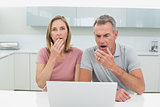 Shocked couple using laptop in kitchen