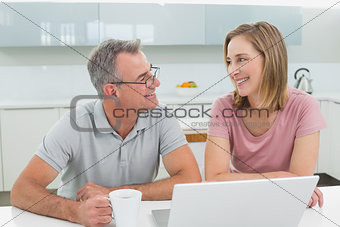 Couple using laptop while man drinking coffee in the kitchen