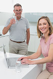 Woman using laptop while man drinking water in kitchen