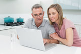 Concentrated couple using laptop in kitchen