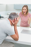 Woman screaming at man as he covers his ears in kitchen