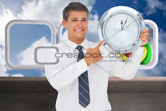 Composite image of anxious businessman holding and showing a clock