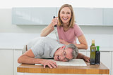 Happy woman holding knife to man's neck in kitchen