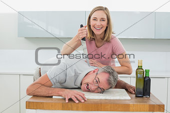 Happy woman holding knife to man's neck in kitchen