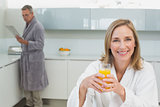 Smiling woman holding orange juice with man in background