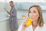 Woman drinking orange juice with man in background