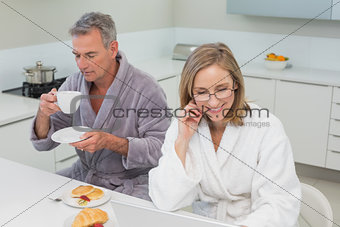 Couple in bathrobes having breakfast in kitchen