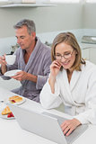 Couple having breakfast while using laptop in kitchen
