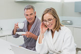 Couple having breakfast while using laptop in kitchen