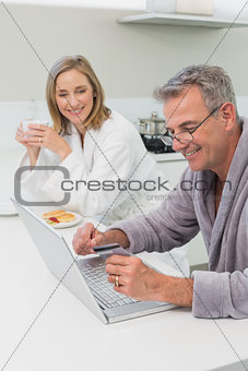 Happy couple in bathrobe doing online shopping at home