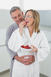 Man embracing woman as she eats strawberry in kitchen