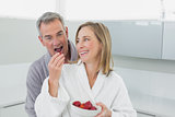 Happy woman feeding man strawberry in kitchen