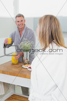 Man offering orange juice to woman in kitchen