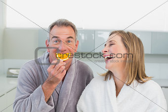 Portrait of a cheerful couple with orange slice in kitchen