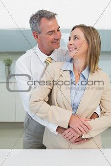 Businessman embracing woman from behind in kitchen