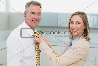 Woman adjusting businessman's tie in kitchen