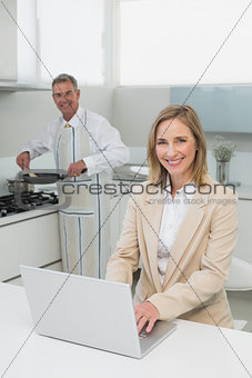 Businesswoman using laptop while man preparing food in kitchen