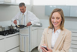 Businesswoman text messaging while man preparing food in kitchen