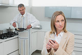 Businesswoman text messaging while man preparing food in kitchen