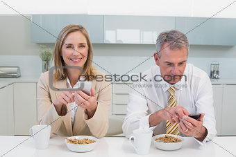Business couple text messaging while having breakfast in kitchen