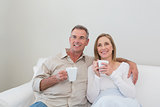 Loving couple with coffee cups looking away in living room