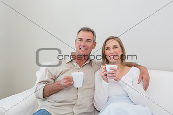 Loving couple with coffee cups looking away in living room