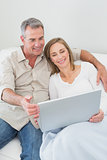 Relaxed couple using laptop on sofa