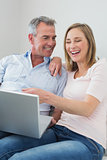 Cheerful couple using laptop on sofa