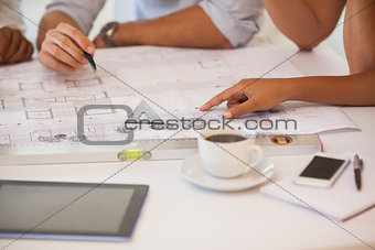 Mid section of business people working on blueprints