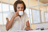 Businesswoman drinking coffee while working on blueprint in office