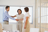 Business people shaking hands besides colleague at office