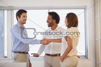 Business people shaking hands besides colleague at office