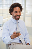 Smiling businessman with mobile phone looking away at office
