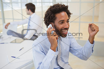 Cheerful businessman using mobile phone at office