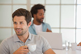 Businessman having coffee with colleague in background