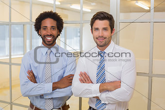 Two smiling businessmen with arms crossed in office