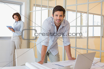Businessman working on blueprints with colleague in background at office