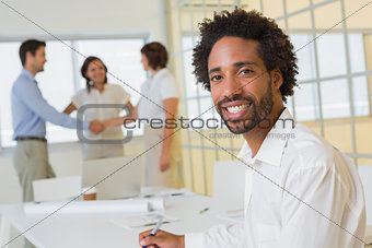 Businessman with colleagues hand shaking in background at office