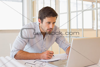 Businessman working on blueprints and laptop in office
