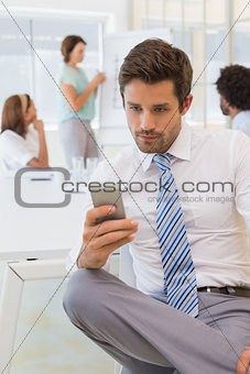 Businessman text messaging with colleagues in meeting
