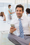 Smiling businessman text messaging with colleagues at office