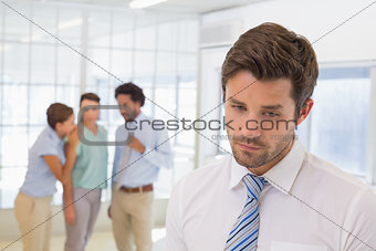 Colleagues gossiping with sad businessman in foreground
