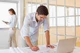 Businessman working on blueprints with colleague in background