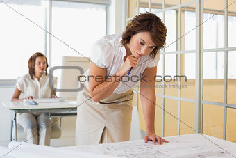 Businesswoman working on blueprints with colleague in background at office