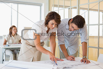 Concentrated colleagues working on blueprints at office