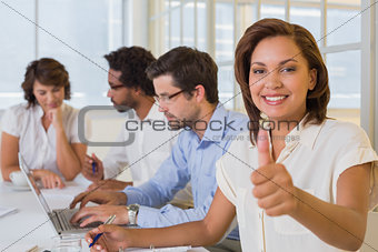 Businesswoman gesturing thumbs up with colleagues in meeting