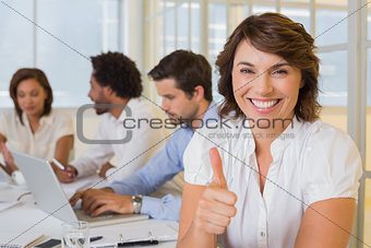 Smiling businesswoman gesturing thumbs up with colleagues in meeting at office