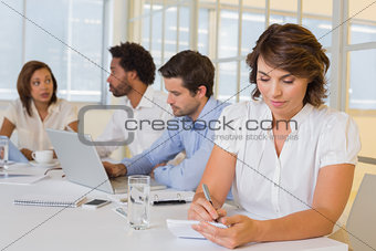 Businesswoman writing notes with colleagues in meeting at office